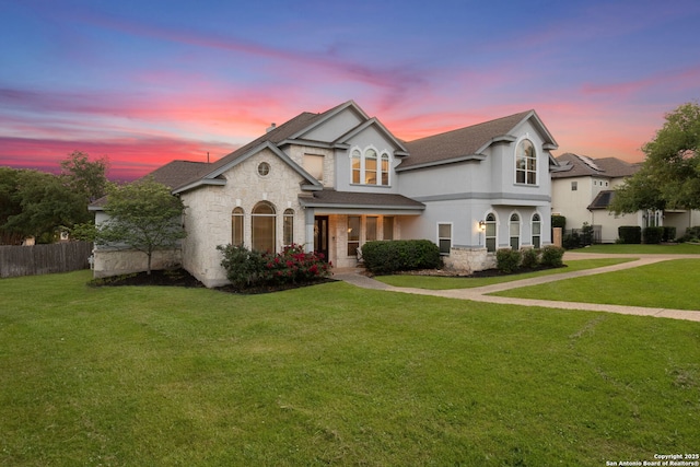 french provincial home with fence, a shingled roof, a front yard, and stone siding