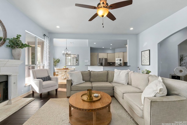 living area featuring recessed lighting, a glass covered fireplace, wood finished floors, and ceiling fan with notable chandelier