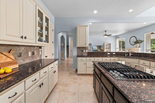 kitchen with a sink, stainless steel gas cooktop, arched walkways, a ceiling fan, and backsplash