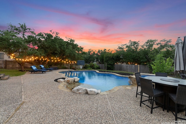 pool at dusk featuring a patio, a fenced in pool, outdoor dining area, and a fenced backyard
