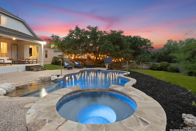 pool at dusk with a fenced backyard, an outdoor hangout area, a pool with connected hot tub, and a patio area