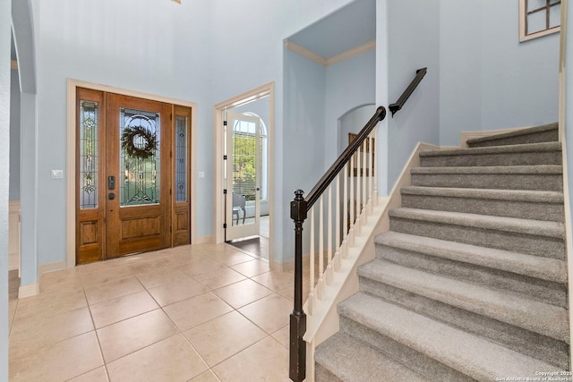 entrance foyer with baseboards, stairs, a towering ceiling, and light tile patterned flooring