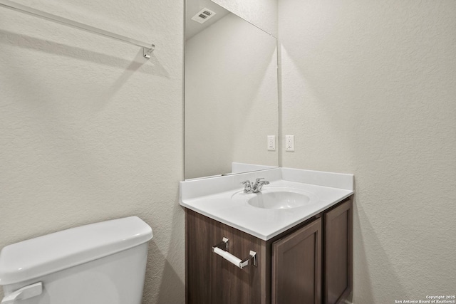 bathroom with vanity, a textured wall, and toilet