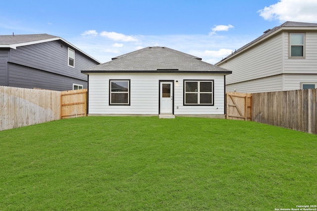 back of property with a fenced backyard, roof with shingles, and a yard