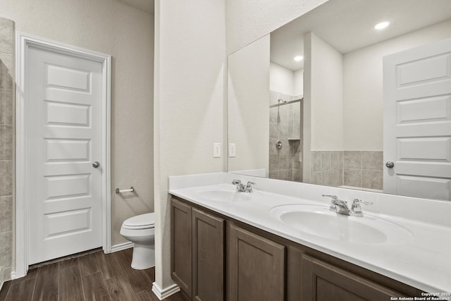 full bath with a sink, toilet, tiled shower, and wood finished floors