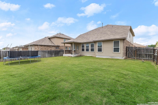 back of house with a yard, brick siding, a fenced backyard, and a trampoline