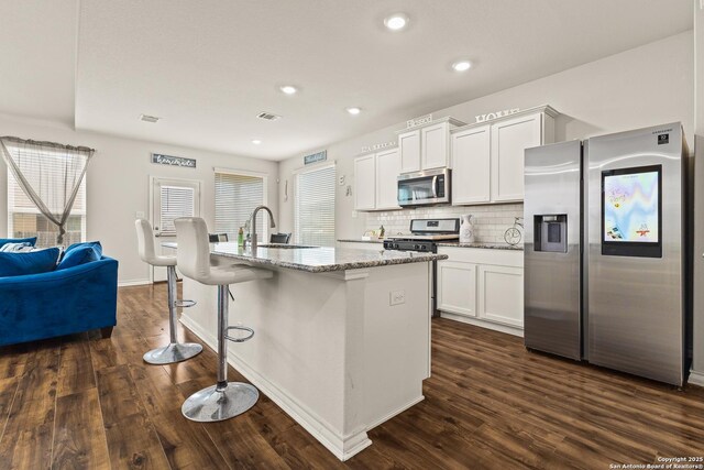 kitchen with visible vents, appliances with stainless steel finishes, dark wood finished floors, a sink, and light stone counters