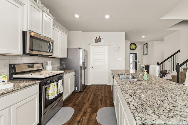 kitchen with appliances with stainless steel finishes, a sink, white cabinetry, backsplash, and dark wood-style floors