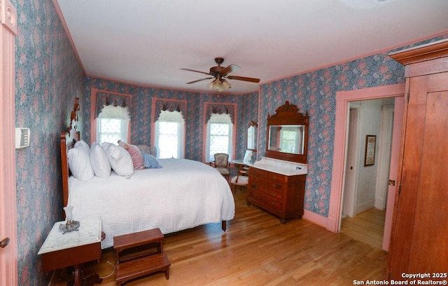 bedroom featuring crown molding, wallpapered walls, baseboards, and light wood-style floors