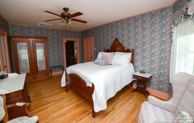 bedroom featuring light wood-style floors, ornamental molding, ceiling fan, and visible vents