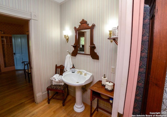 bathroom featuring baseboards, wallpapered walls, and wood finished floors
