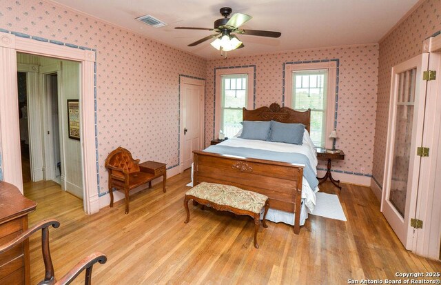bedroom featuring light wood-style floors, crown molding, visible vents, and wallpapered walls