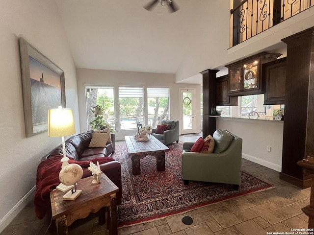 living area with baseboards, ceiling fan, lofted ceiling, and stone finish floor