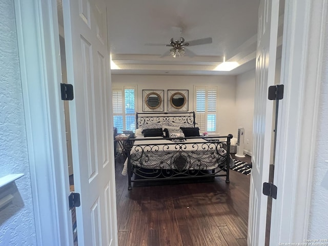 bedroom with a raised ceiling, wood-type flooring, and a ceiling fan
