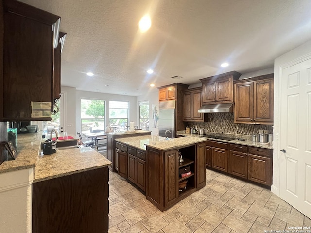 kitchen featuring black electric stovetop, recessed lighting, backsplash, under cabinet range hood, and built in refrigerator