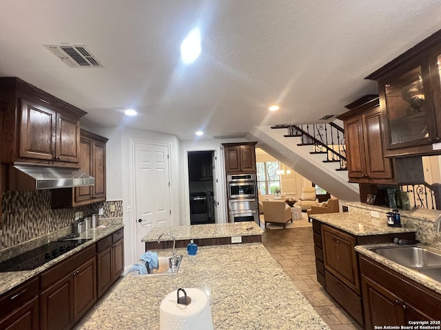 kitchen with under cabinet range hood, black electric cooktop, visible vents, and a sink