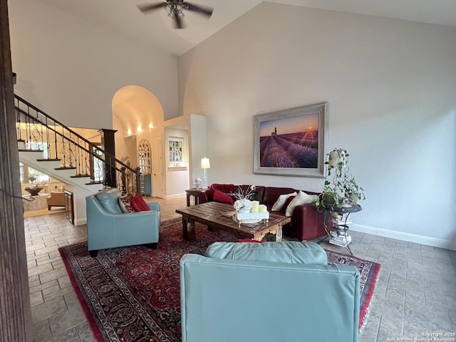 living room featuring ceiling fan, arched walkways, stairway, baseboards, and stone tile flooring