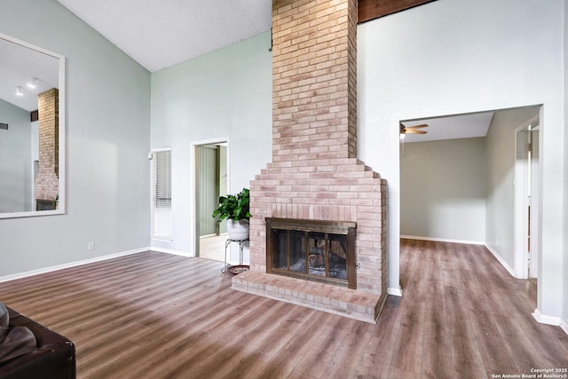 unfurnished living room with ceiling fan, a brick fireplace, high vaulted ceiling, baseboards, and wood finished floors