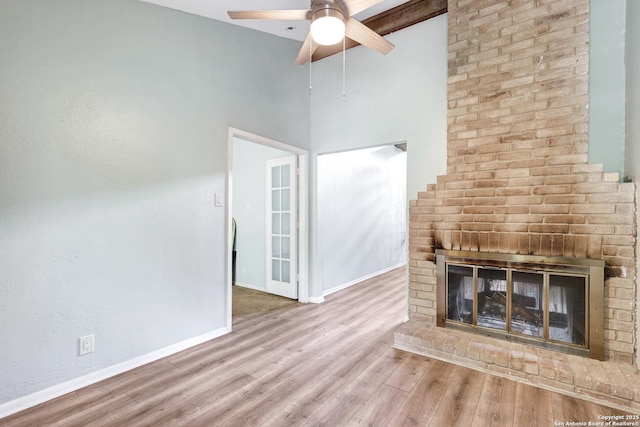 unfurnished living room with wood finished floors, a fireplace, baseboards, a high ceiling, and a ceiling fan