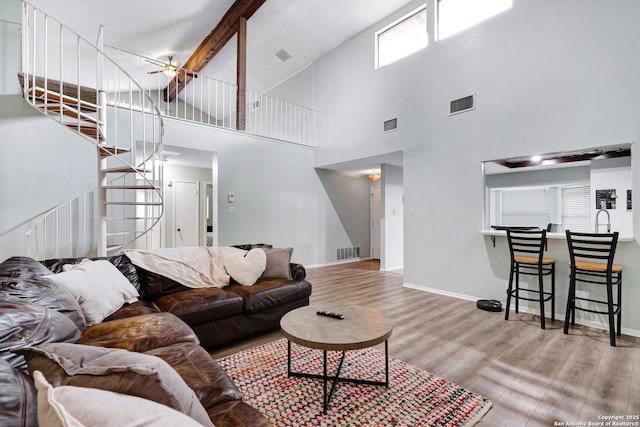 living room featuring stairs, a high ceiling, visible vents, and wood finished floors