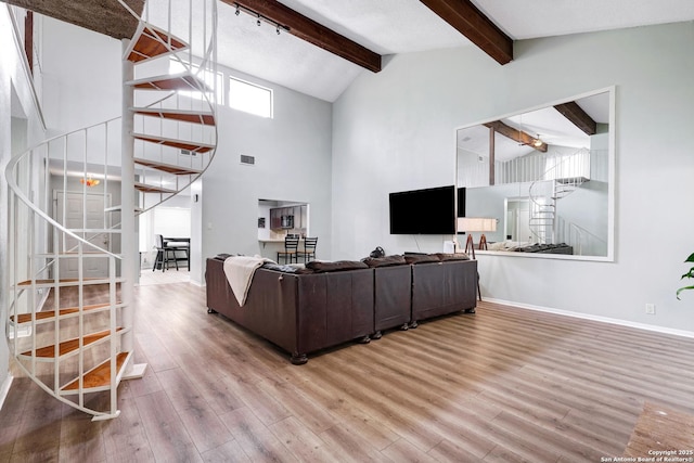 living room featuring stairs, beamed ceiling, baseboards, high vaulted ceiling, and light wood-type flooring