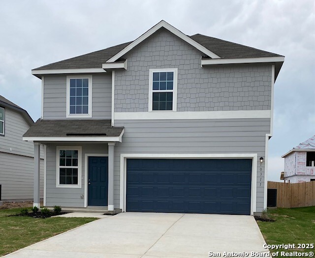 traditional home with an attached garage, a shingled roof, fence, and driveway