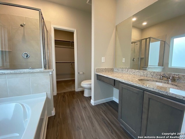 full bath featuring vanity, a shower stall, wood finished floors, a spacious closet, and a garden tub