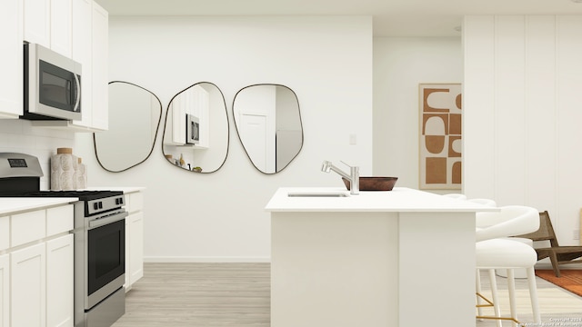 kitchen with stainless steel range with gas stovetop, a breakfast bar, a sink, and light wood-style floors