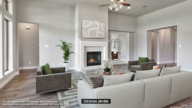 living area with ceiling fan, a towering ceiling, visible vents, baseboards, and a glass covered fireplace