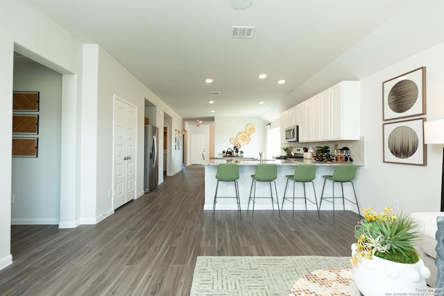 kitchen featuring appliances with stainless steel finishes, a peninsula, white cabinetry, dark wood-type flooring, and visible vents
