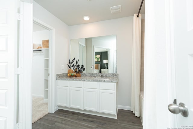 full bath featuring a walk in closet, shower / bath combo, wood finished floors, vanity, and baseboards