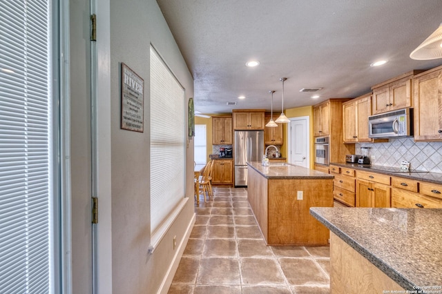 kitchen featuring appliances with stainless steel finishes, an island with sink, recessed lighting, decorative backsplash, and visible vents