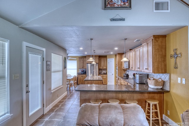 kitchen featuring visible vents, freestanding refrigerator, decorative backsplash, baseboards, and an island with sink