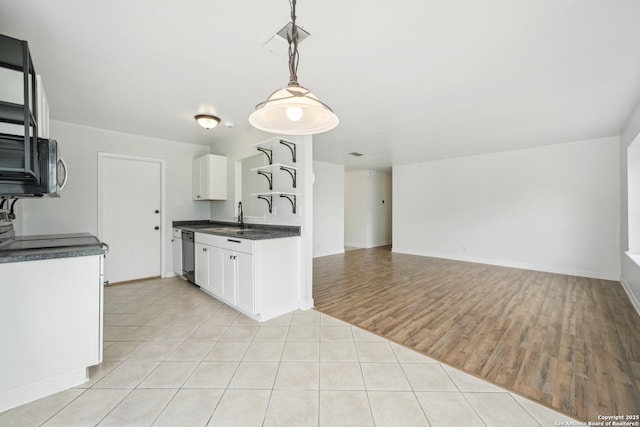 kitchen featuring dark countertops, a sink, white cabinetry, light tile patterned floors, and stainless steel dishwasher