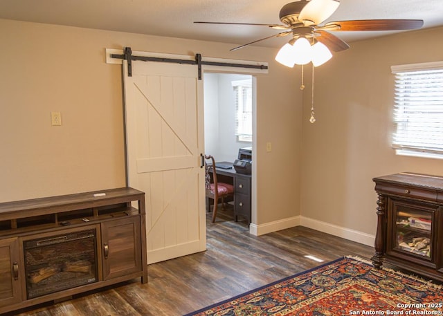 interior space with baseboards, ceiling fan, dark wood-style floors, and a barn door
