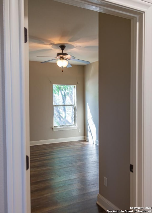 empty room with baseboards, a ceiling fan, and dark wood-style floors
