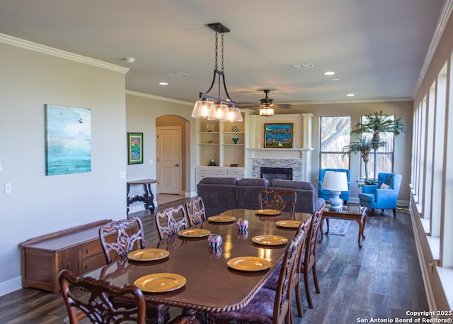 dining room with a ceiling fan, arched walkways, a fireplace, dark wood-style floors, and ornamental molding
