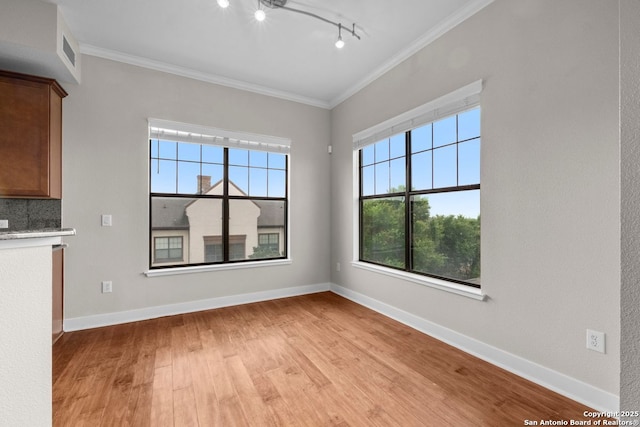 unfurnished dining area with baseboards, ornamental molding, light wood finished floors, and a healthy amount of sunlight