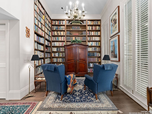sitting room with wall of books, crown molding, wood finished floors, baseboards, and a chandelier