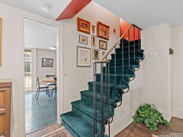 staircase with baseboards, wood finished floors, and visible vents