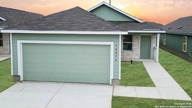 view of front of home with roof with shingles, an attached garage, stone siding, concrete driveway, and a lawn