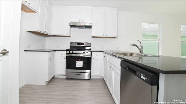 kitchen with dark countertops, appliances with stainless steel finishes, a sink, a peninsula, and under cabinet range hood