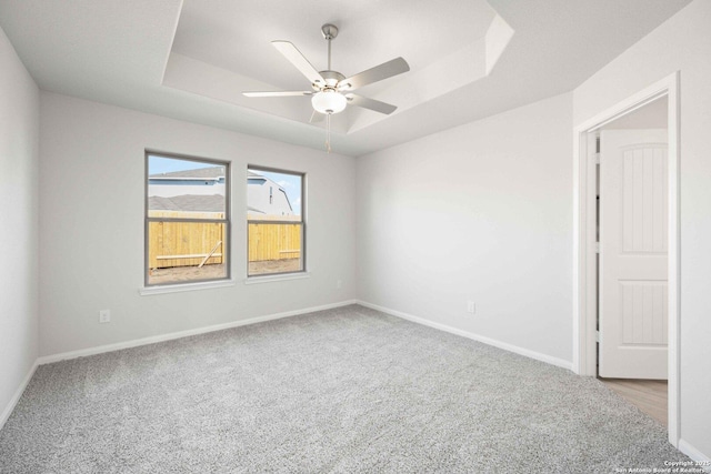 carpeted spare room featuring a ceiling fan, baseboards, and a raised ceiling