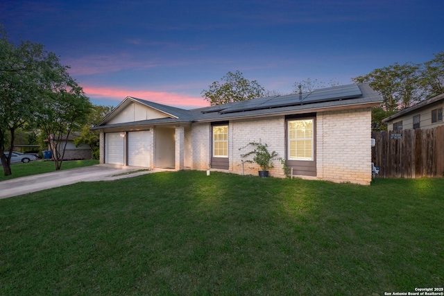 ranch-style house featuring driveway, a front lawn, roof mounted solar panels, and a garage