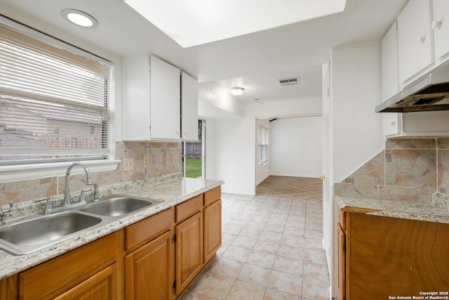 kitchen featuring visible vents, light countertops, under cabinet range hood, a sink, and backsplash