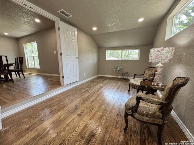 living area with a textured ceiling, visible vents, hardwood / wood-style flooring, baseboards, and a textured wall