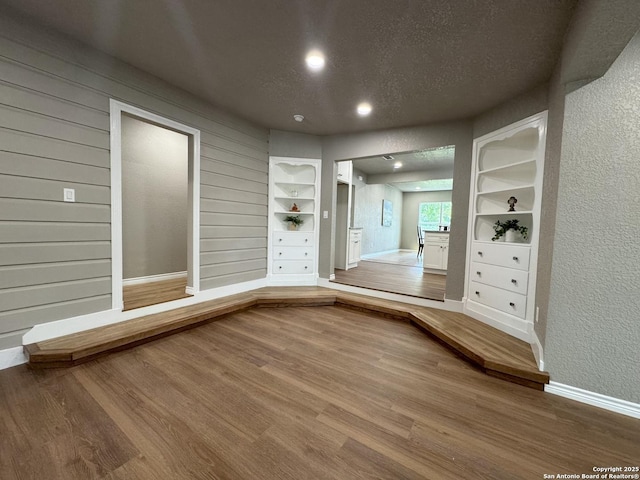 interior space with built in features, wood finished floors, baseboards, a textured wall, and recessed lighting