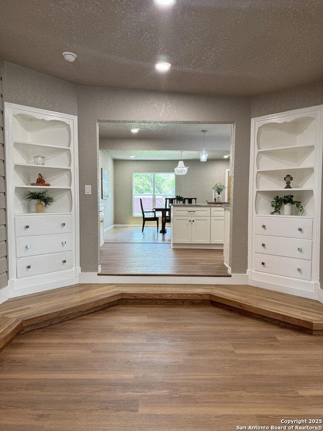 interior space featuring a textured ceiling, built in shelves, recessed lighting, baseboards, and wood finished floors
