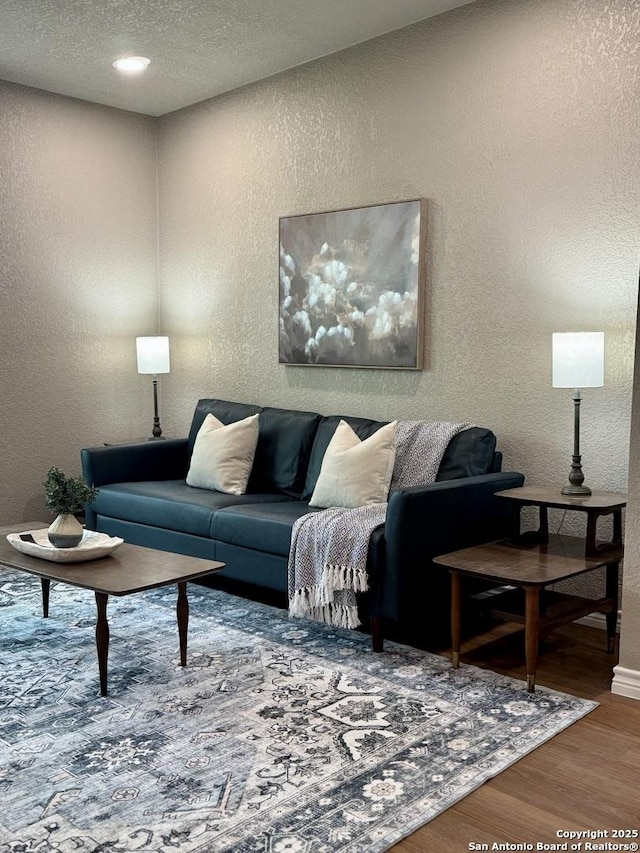 living area with baseboards, a textured wall, and wood finished floors