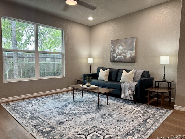 living area featuring a ceiling fan, a textured wall, a textured ceiling, and wood finished floors